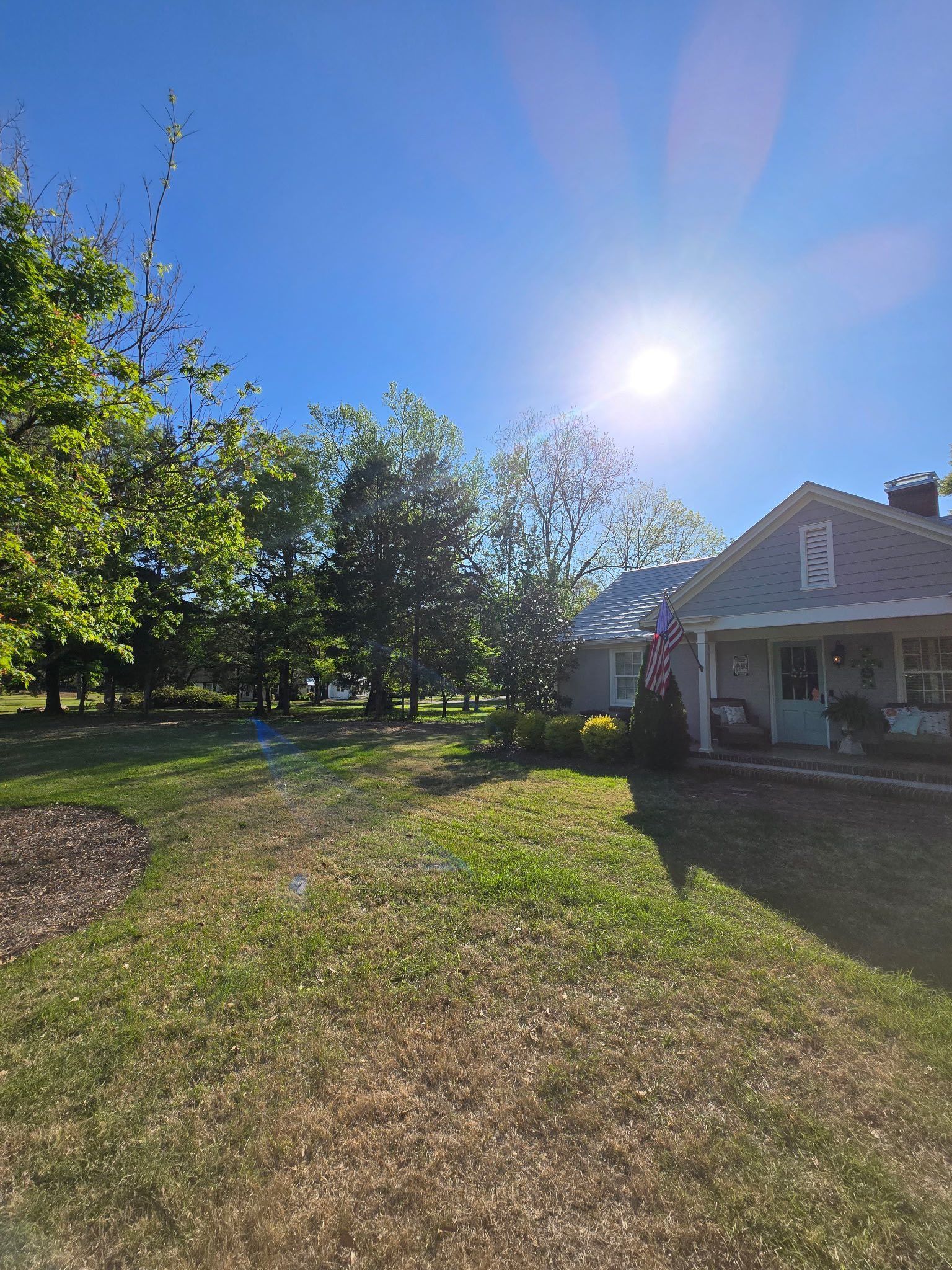 A house with a porch and a flag in front of it on a sunny day.