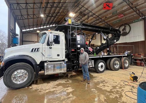 A man is standing in front of a large truck in a garage. A man is standing in front of a large truck in a garage.