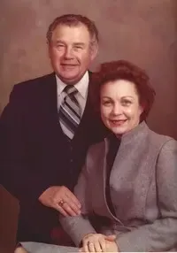 Couple posing for a portrait. Man in suit, woman in gray blazer, both smiling.