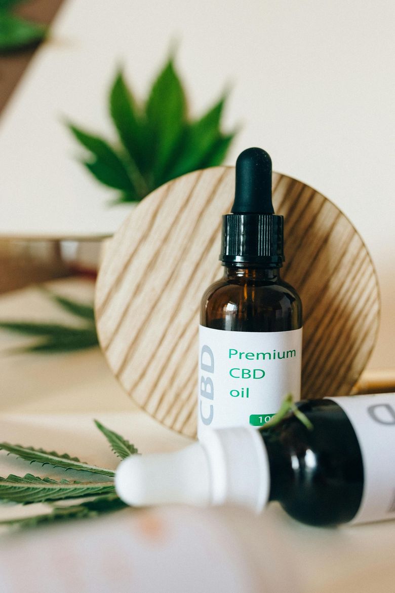 Two CBD oil bottles with droppers, on a wooden surface, with hemp leaves in the background.