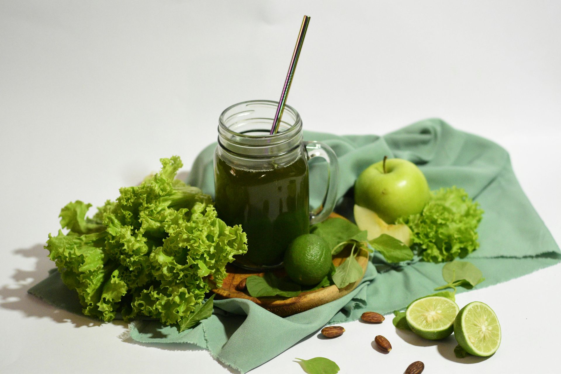 Green smoothie in a mason jar with fruit and lettuce on a green cloth.