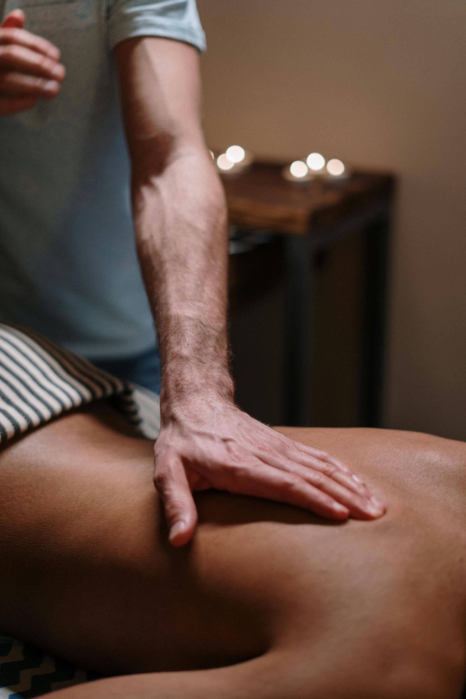 Person receiving back massage, dark setting. Therapist's hand on the lower back.