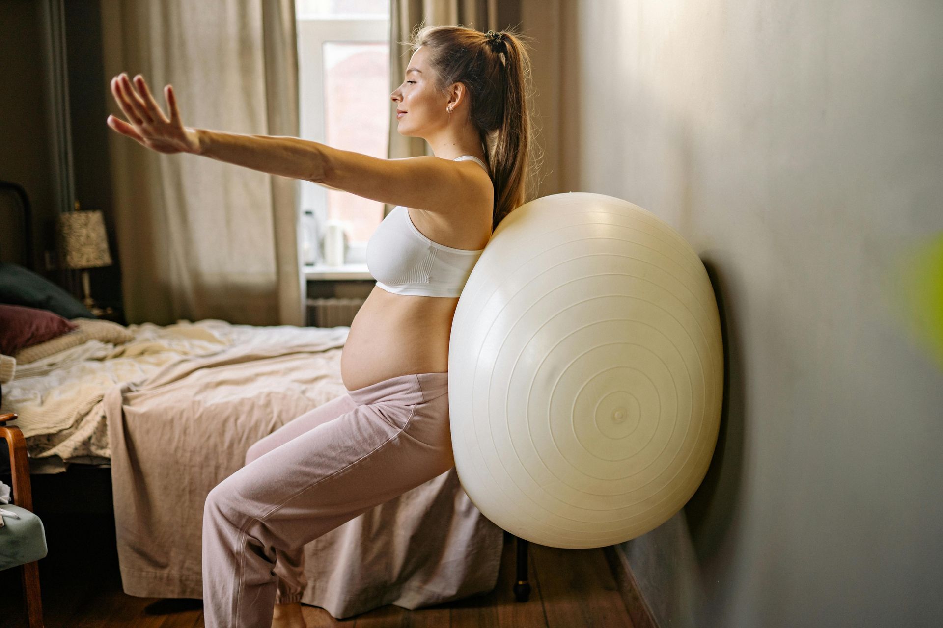 Pregnant woman doing exercise with a stability ball against a wall, arms out.