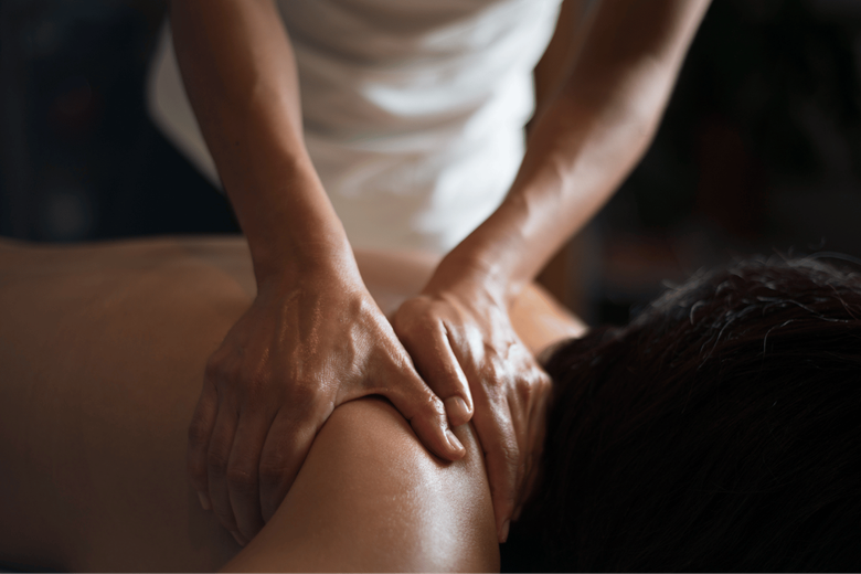 Hands of masseuse massaging a person's lower back, draped with white towel.