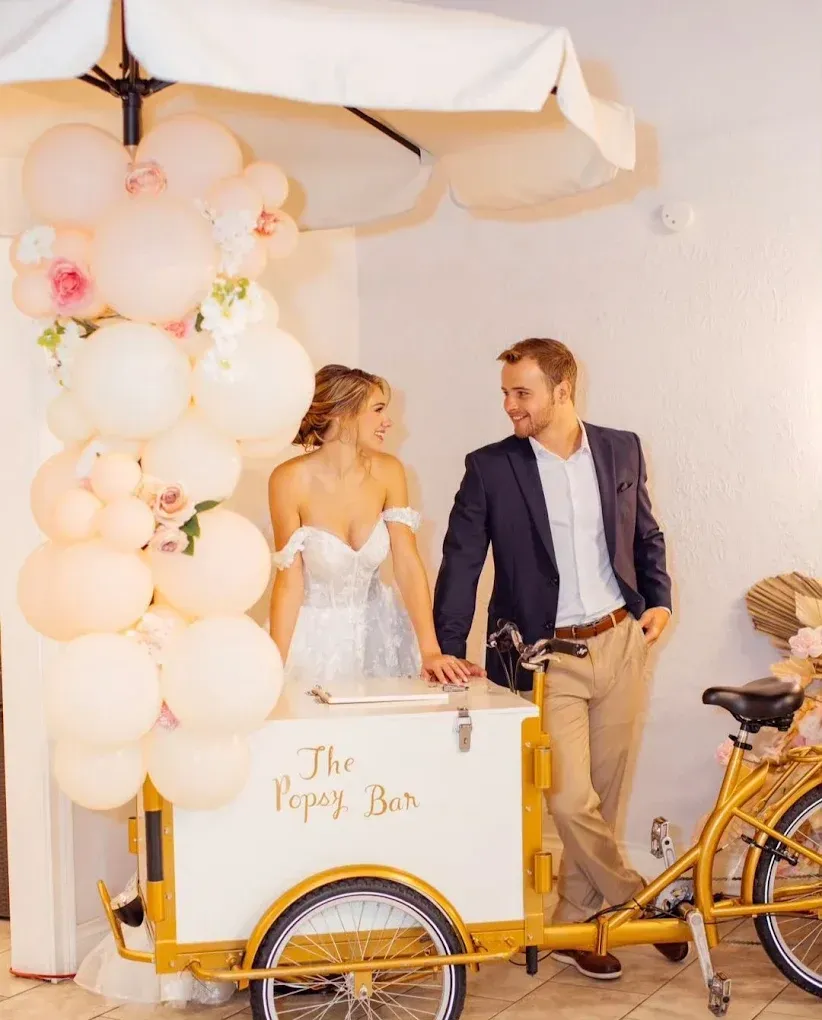 Bride and groom near a popcorn bar at their wedding. Soft pink and gold decor with the couple holding drinks.