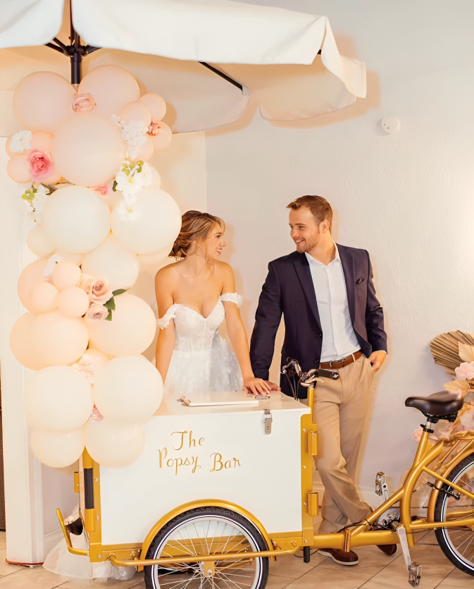 Bride and groom near a popcorn bar at their wedding. Soft pink and gold decor with the couple holding drinks.