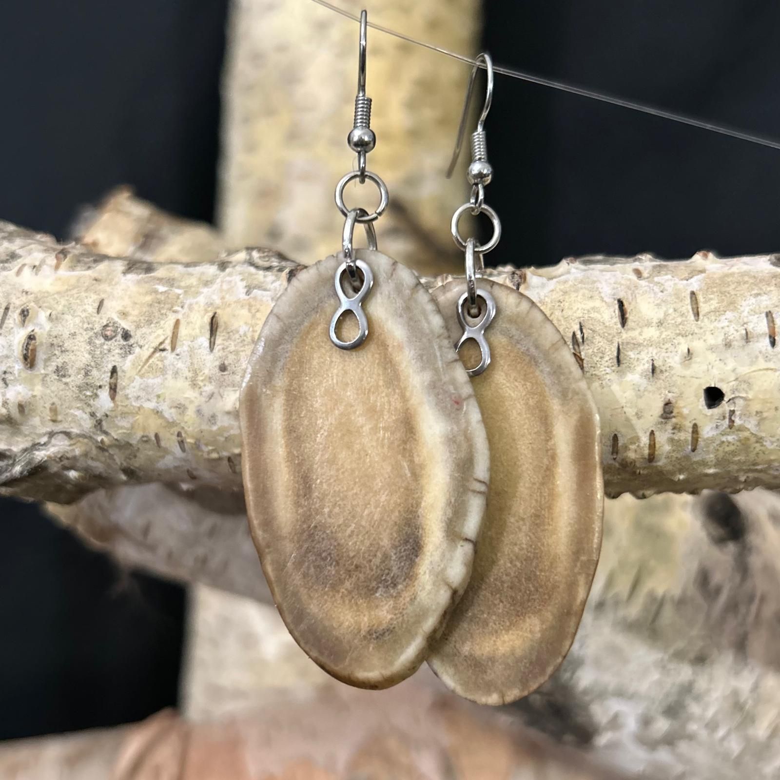 Deer antler slice earrings with a small silver Metis charm.
