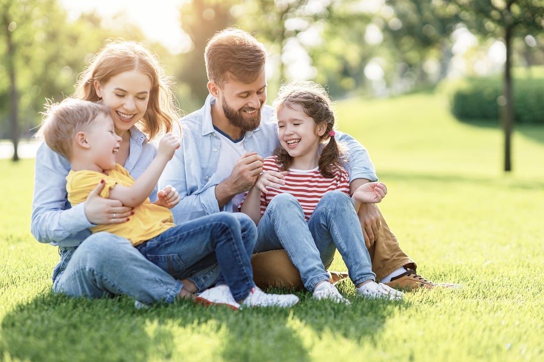Family laughing together on grass in a park. Sunlit.