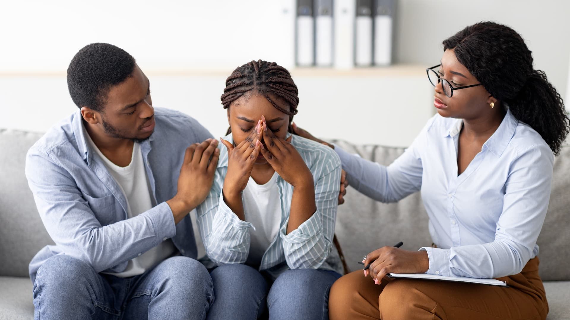 Couple in therapy, woman crying while the therapist and man console her.
