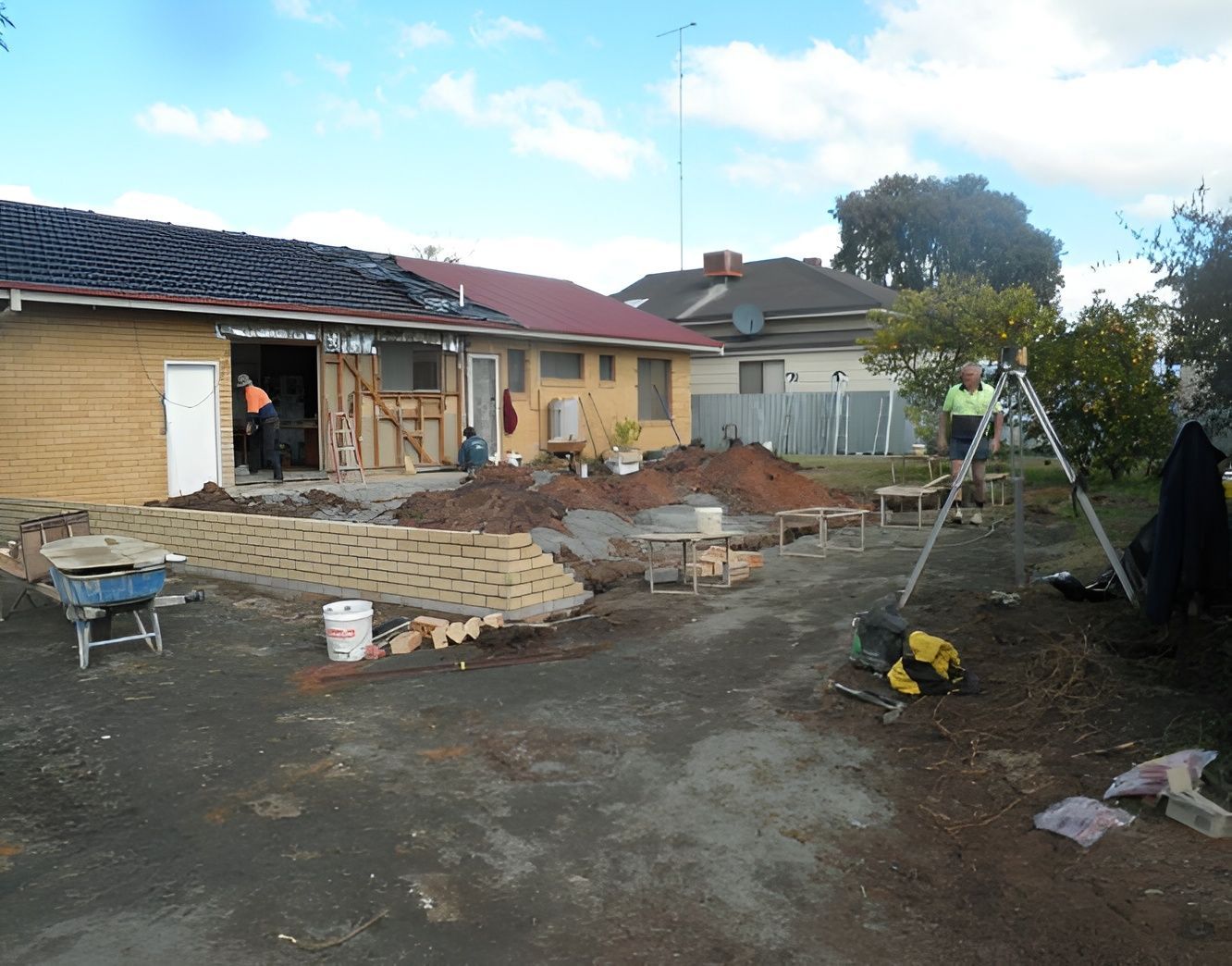 Workers renovating the exterior of a suburban house with a partially exposed frame and a brick retaining wall. — Daniher Building Company in Yass, NSW