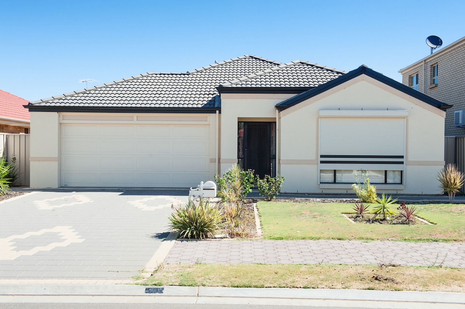 A single-story, beige suburban house with a two-car garage, a tiled roof, and a front window with a closed roller shutter. — Daniher Building Company in Belconnen, ACT