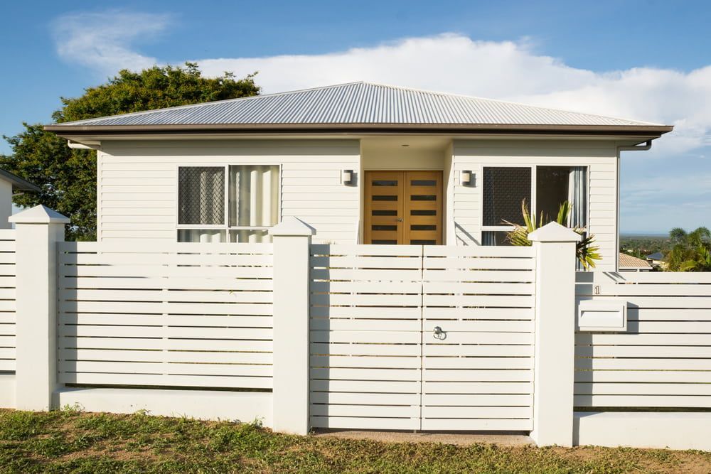 A Single-story White House With a Metal Roof and a Matching White Slatted Fence — Daniher Building Company in Yass, NSW