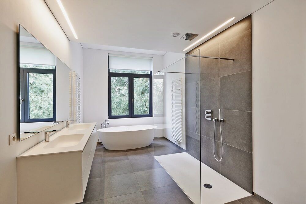 A modern bathroom featuring a white double vanity, a freestanding oval bathtub, and a large, glass-enclosed shower. — Daniher Building Company in Flynn, ACT