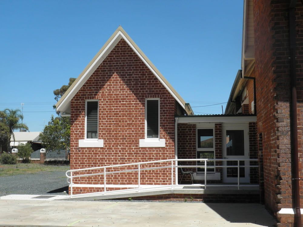A red brick building features a white wheelchair ramp leading to a glass-paned doorway under a bright blue sky. — Daniher Building Company in Flynn, ACT