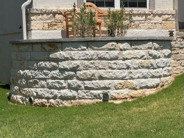 A stone wall in front of a house with a chair in the background