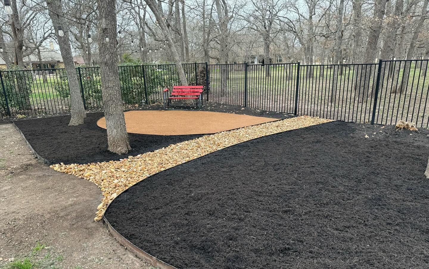 A red bench is sitting in the middle of a garden surrounded by trees.