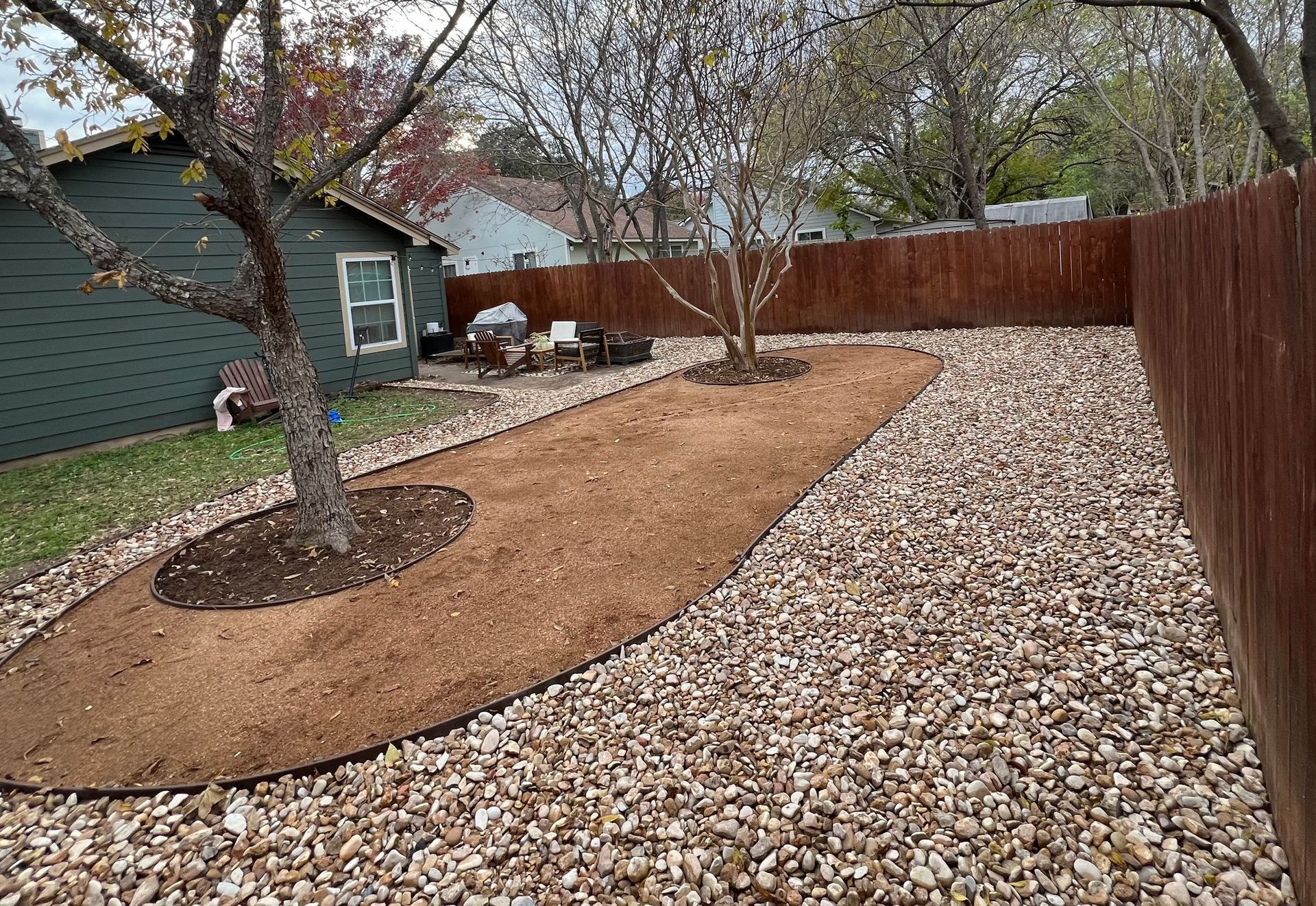 A backyard with a fence and a tree in the middle of it.
