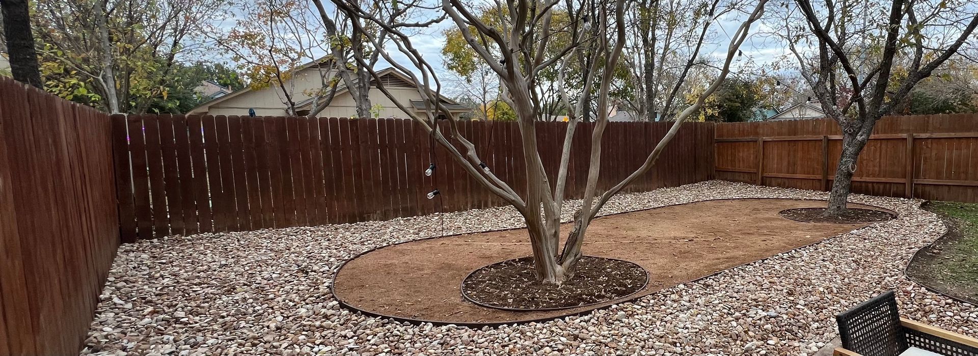 A backyard with a wooden fence and a tree in the middle of it.