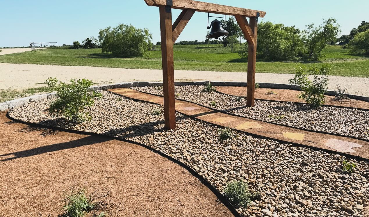 A wooden pergola is sitting in the middle of a gravel path.