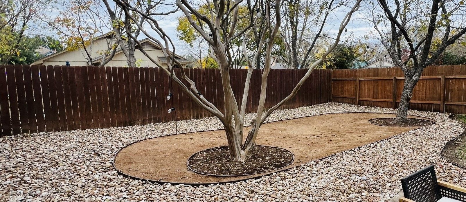 A backyard with a wooden fence and a tree in the middle of it.