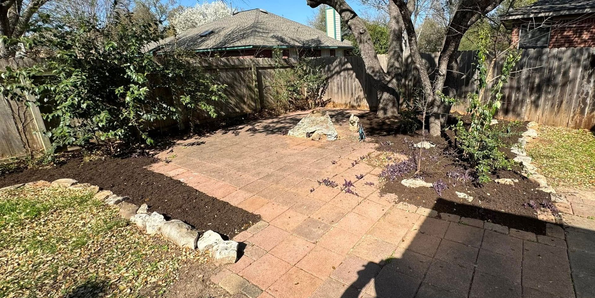 A brick patio in the backyard of a house surrounded by trees and bushes.