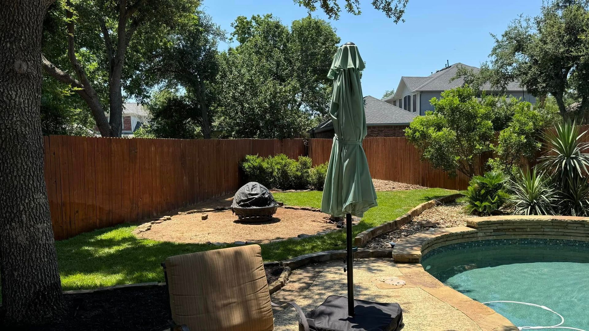 There is a swimming pool in the backyard with a chair and umbrella.