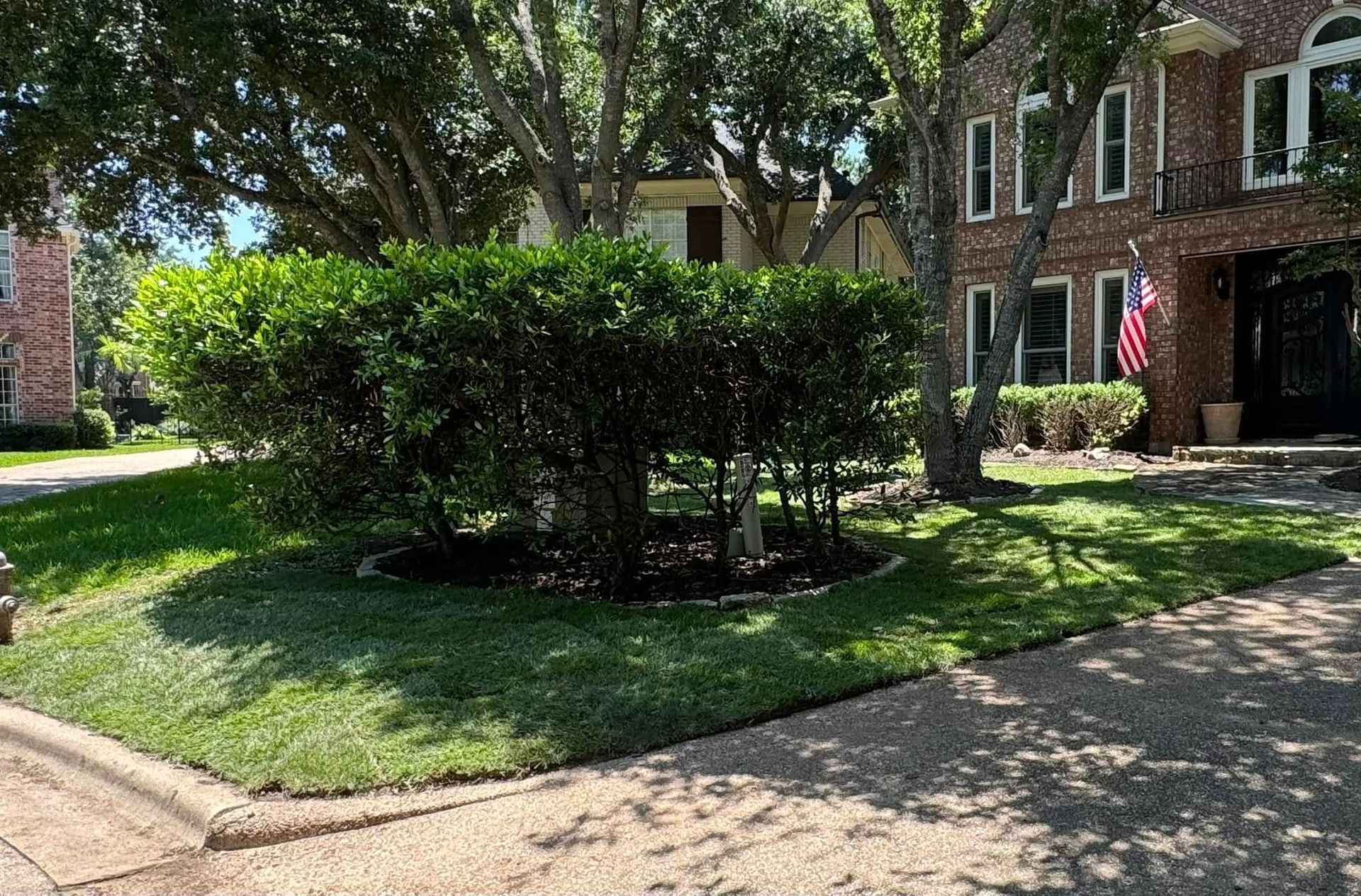 A brick house with a lush green lawn and bushes in front of it.