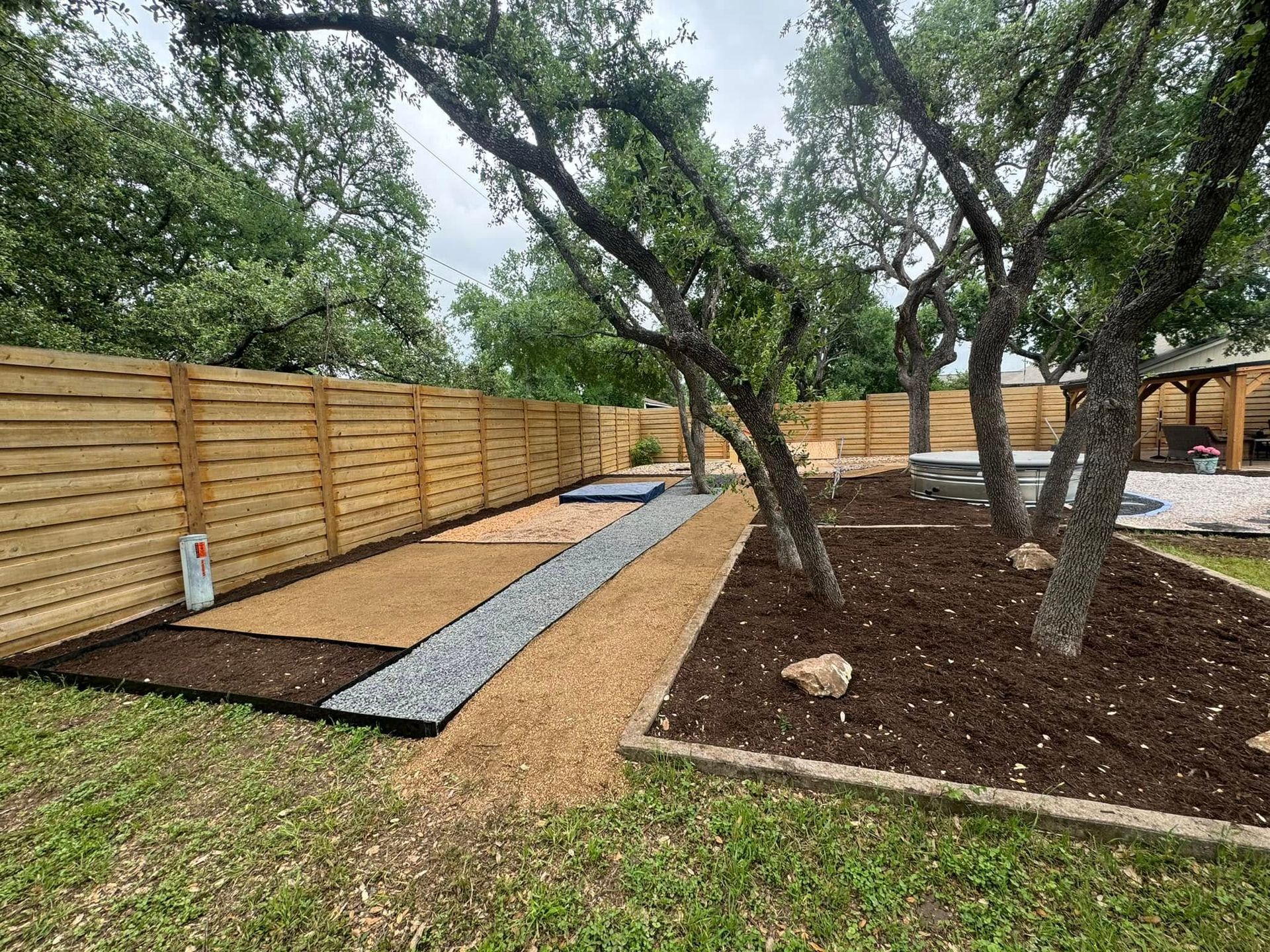 A wooden fence surrounds a lush green yard with trees.