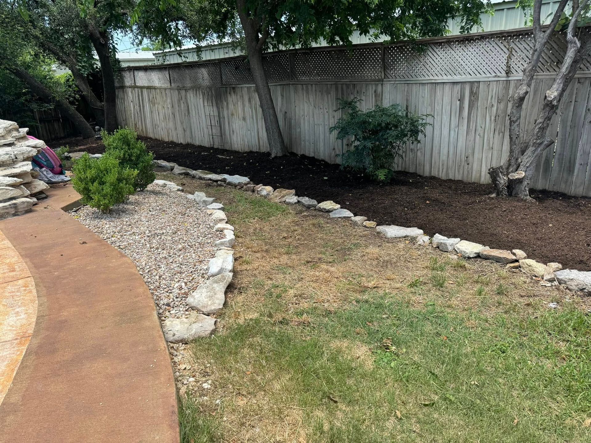 A backyard with a stone walkway and a wooden fence.