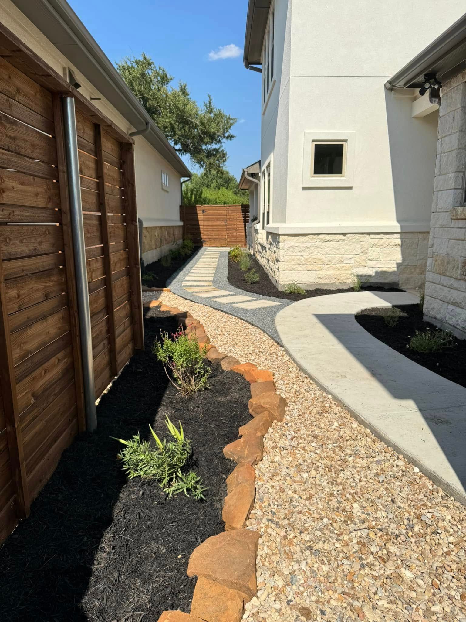 A walkway leading to a house with a wooden fence and gravel.
