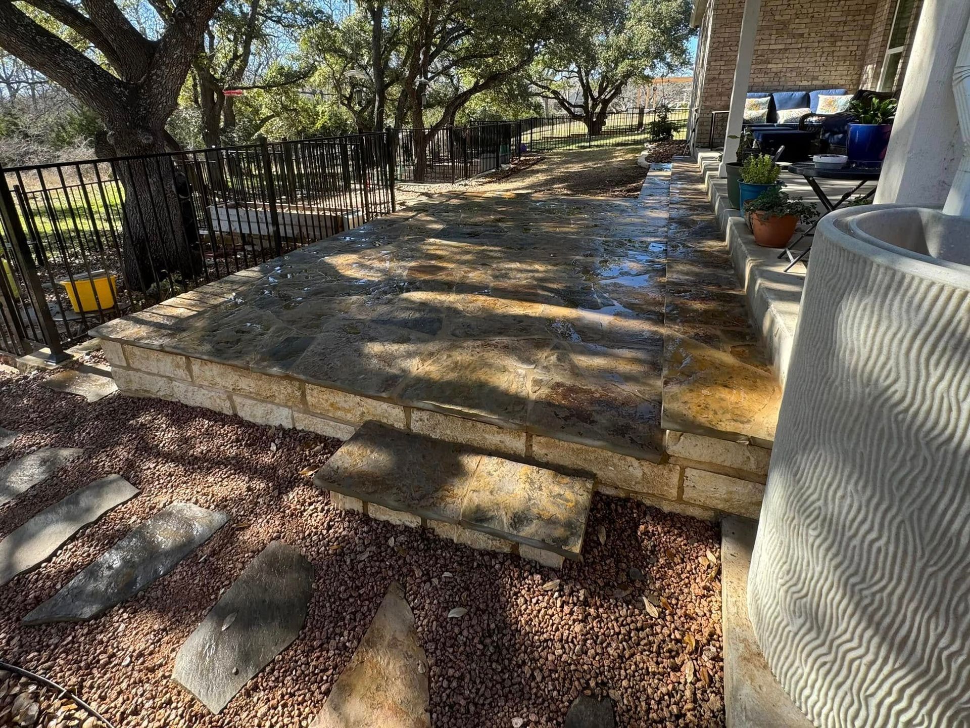 A stone walkway leading to a porch with trees in the background.