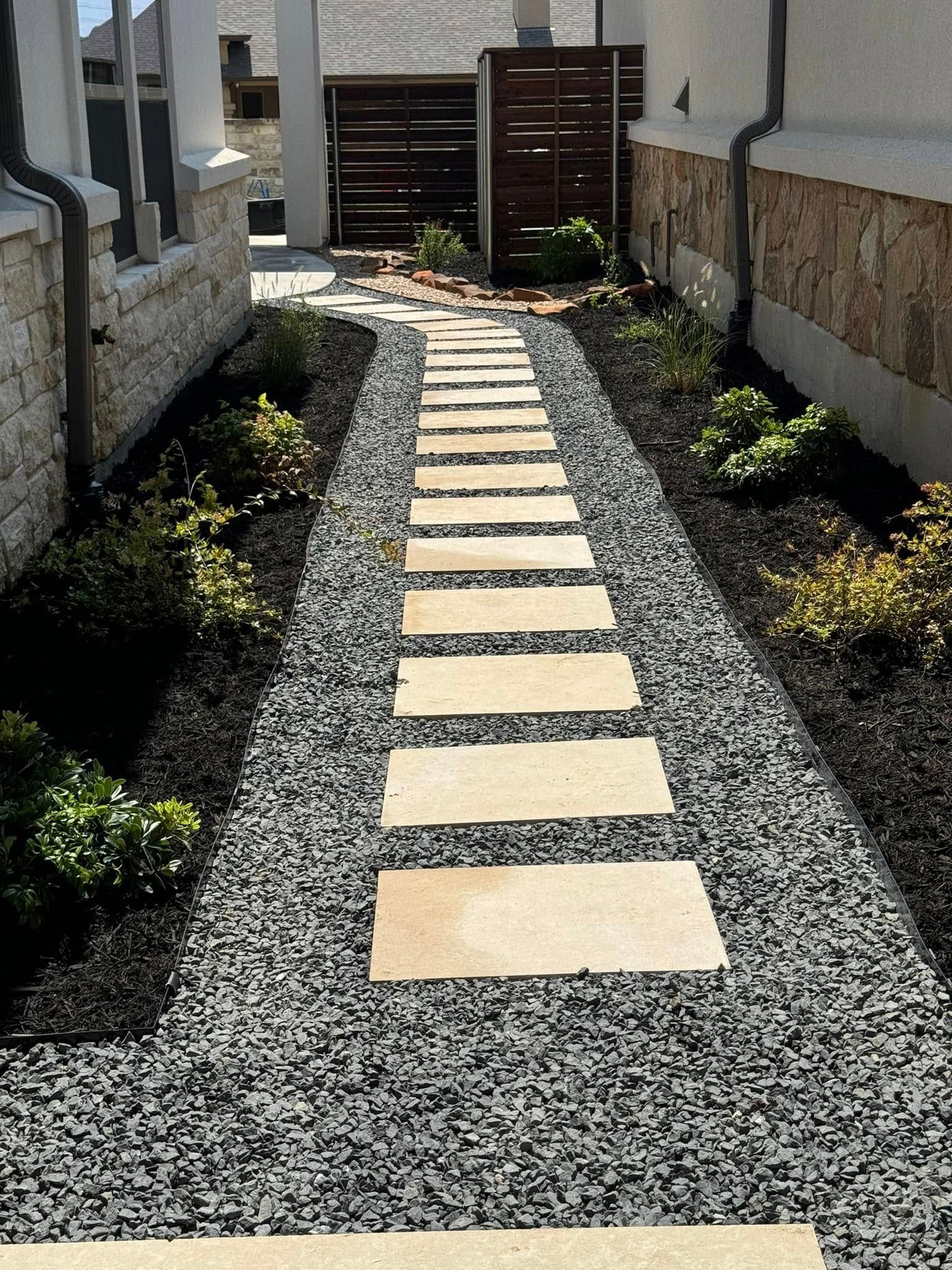 A stone walkway leading to a house with gravel and plants.