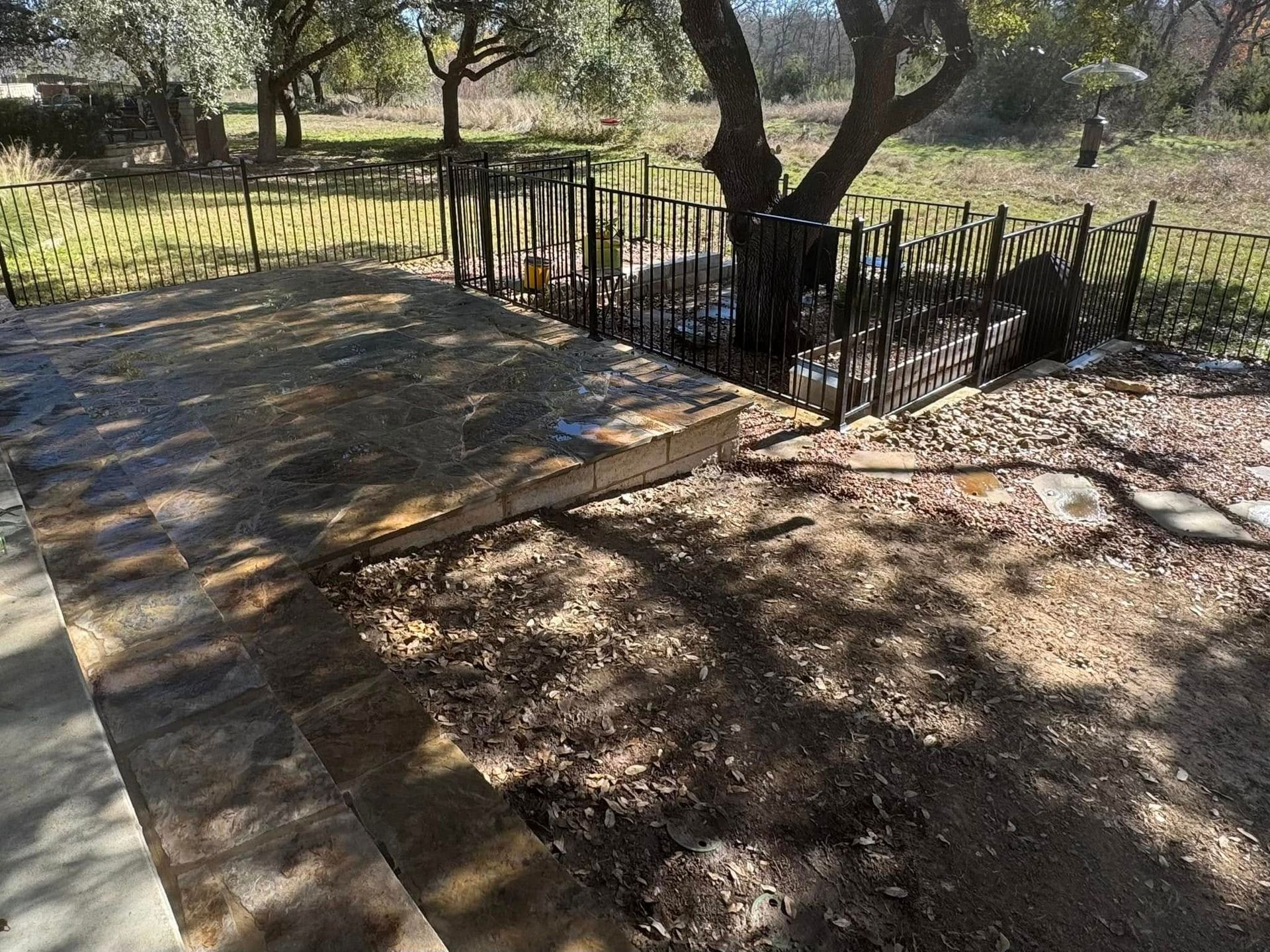 A stone walkway leading to a fenced in yard with trees in the background.
