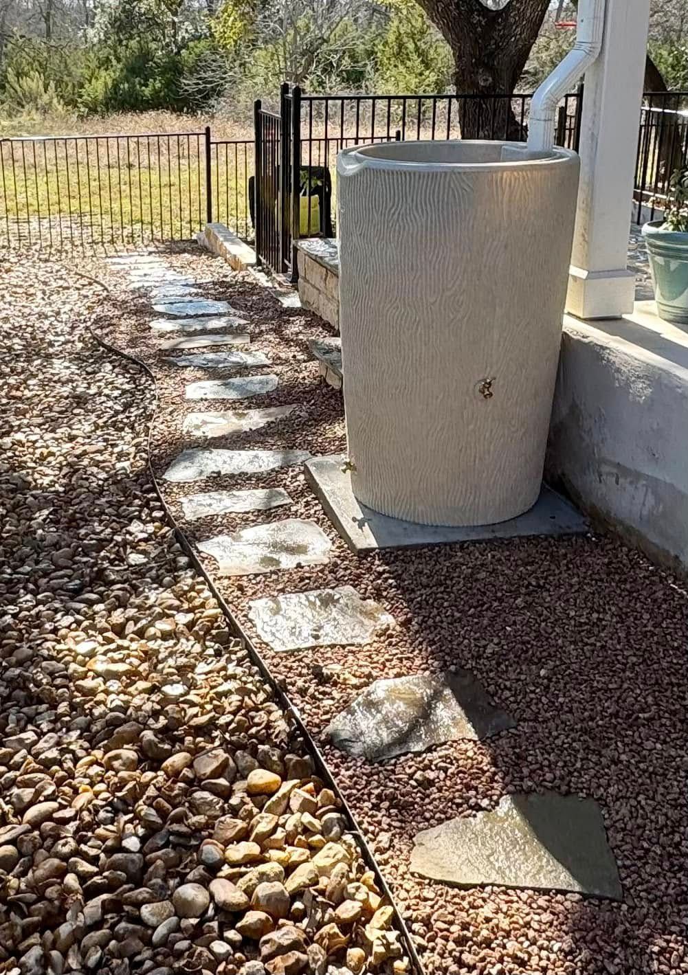 A white rain barrel is sitting on top of a gravel path.