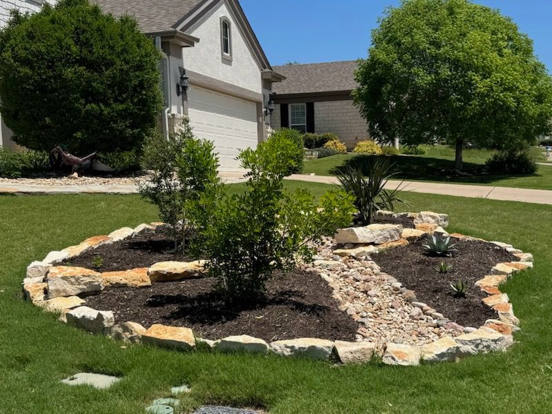A circular garden with rocks and plants in front of a house. Landscaping done by Labay Landscaping LLC.