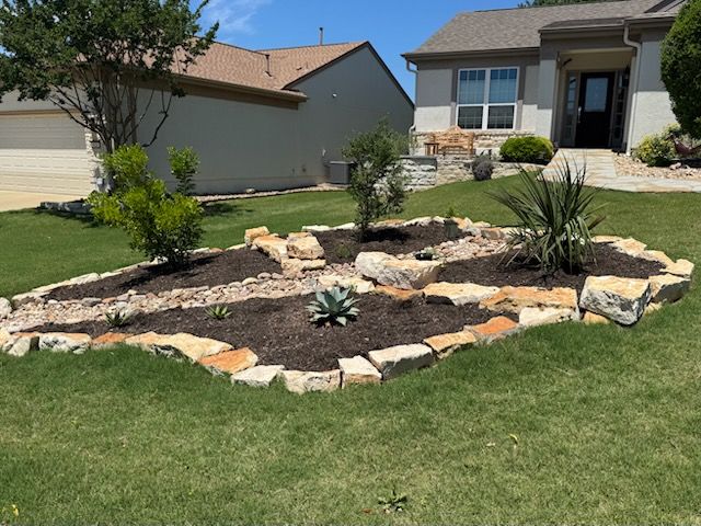 A house with a lush green lawn and a rock garden in front of it.