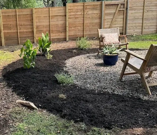 A small tree is growing in a wooden planter in front of a wooden fence.