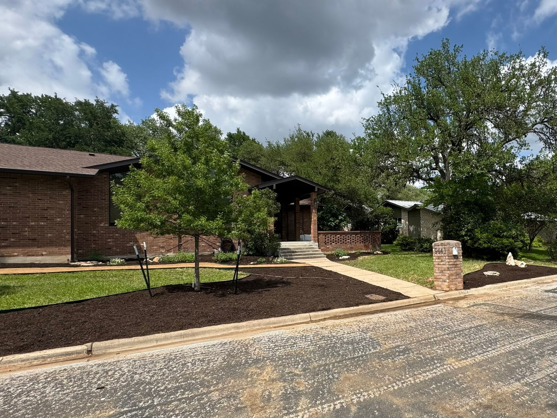 A brick house with a lush green lawn and trees in front of it.