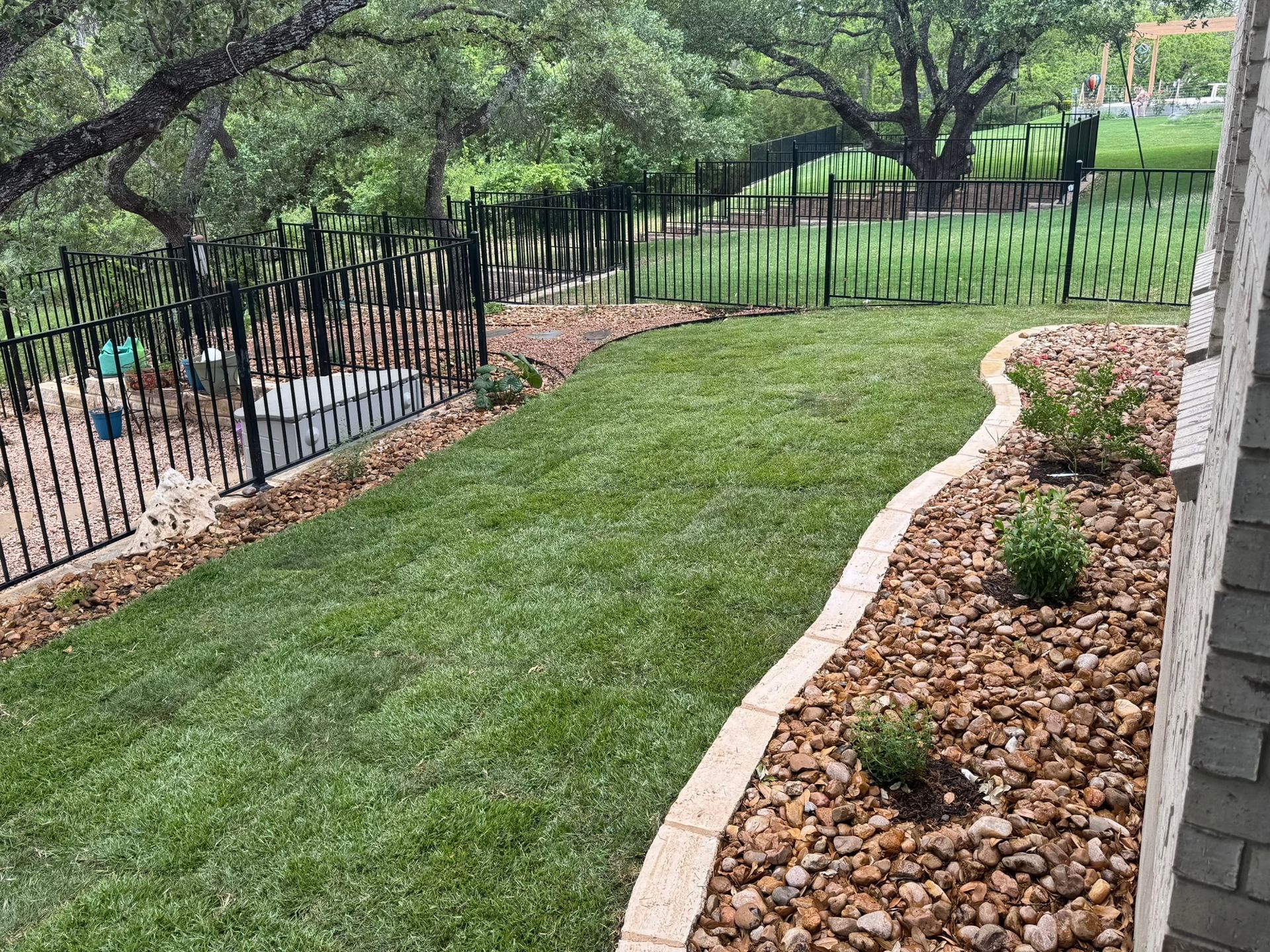A backyard with a fence and a lush green lawn.