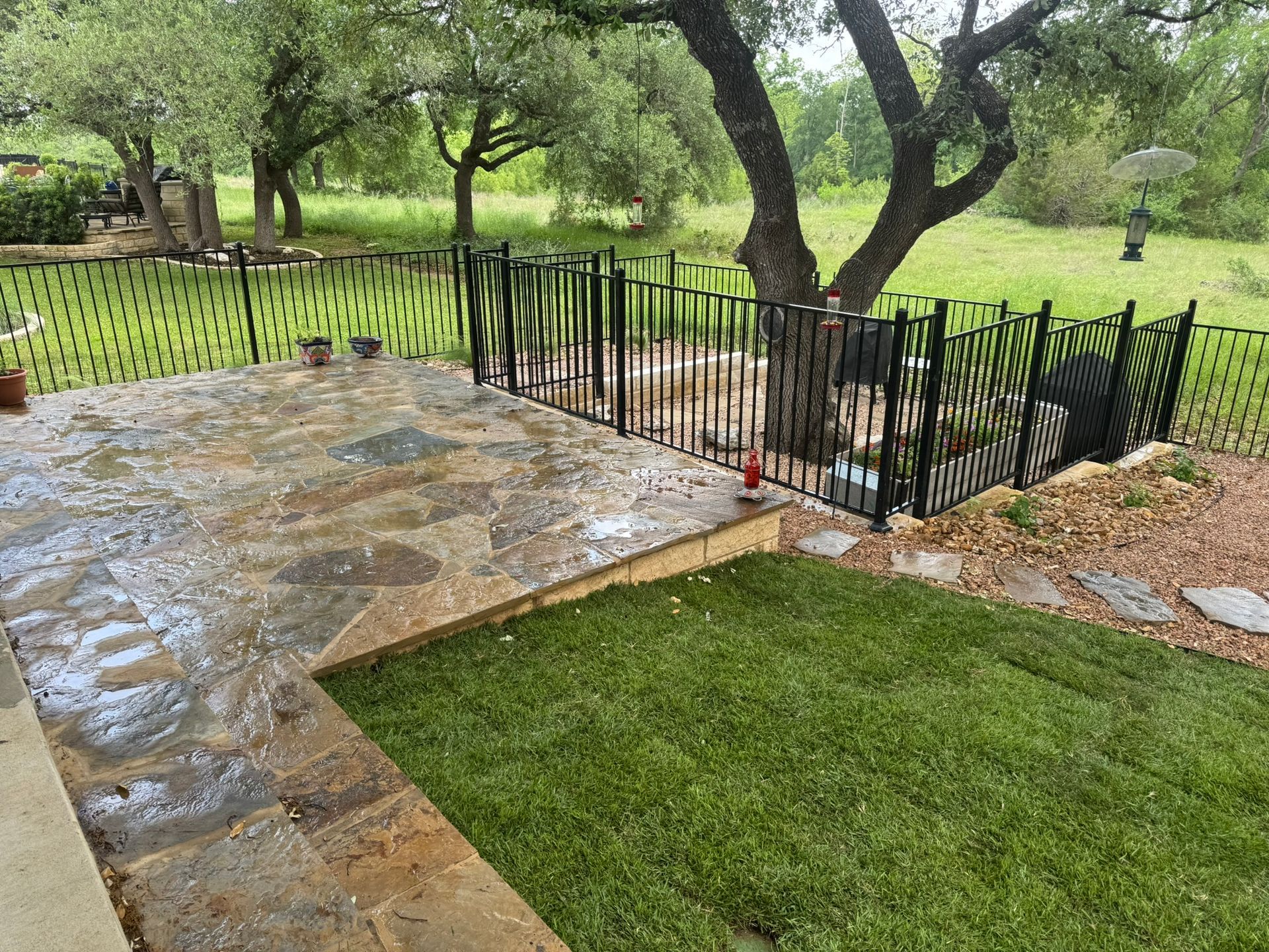 A stone patio with a metal fence and a tree in the background.