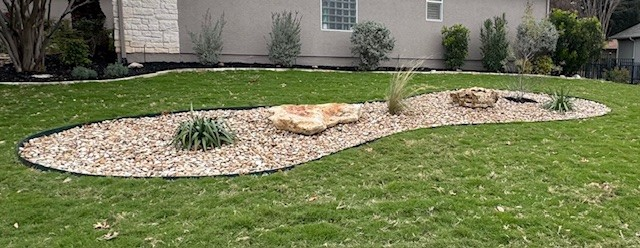 A decorative landscaping bed in a yard with gravel, rocks, and plants.