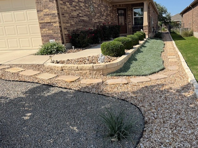 Front yard landscaping with gravel, stone pathway, and trimmed shrubs bordering a house.