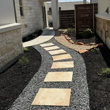 Stone path with stepping stones through a landscaped yard with black gravel and mulch.