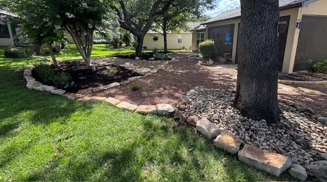 Landscaped backyard with mulch, rocks, and a tree. Lawn in foreground, pathway in middle, house in background.