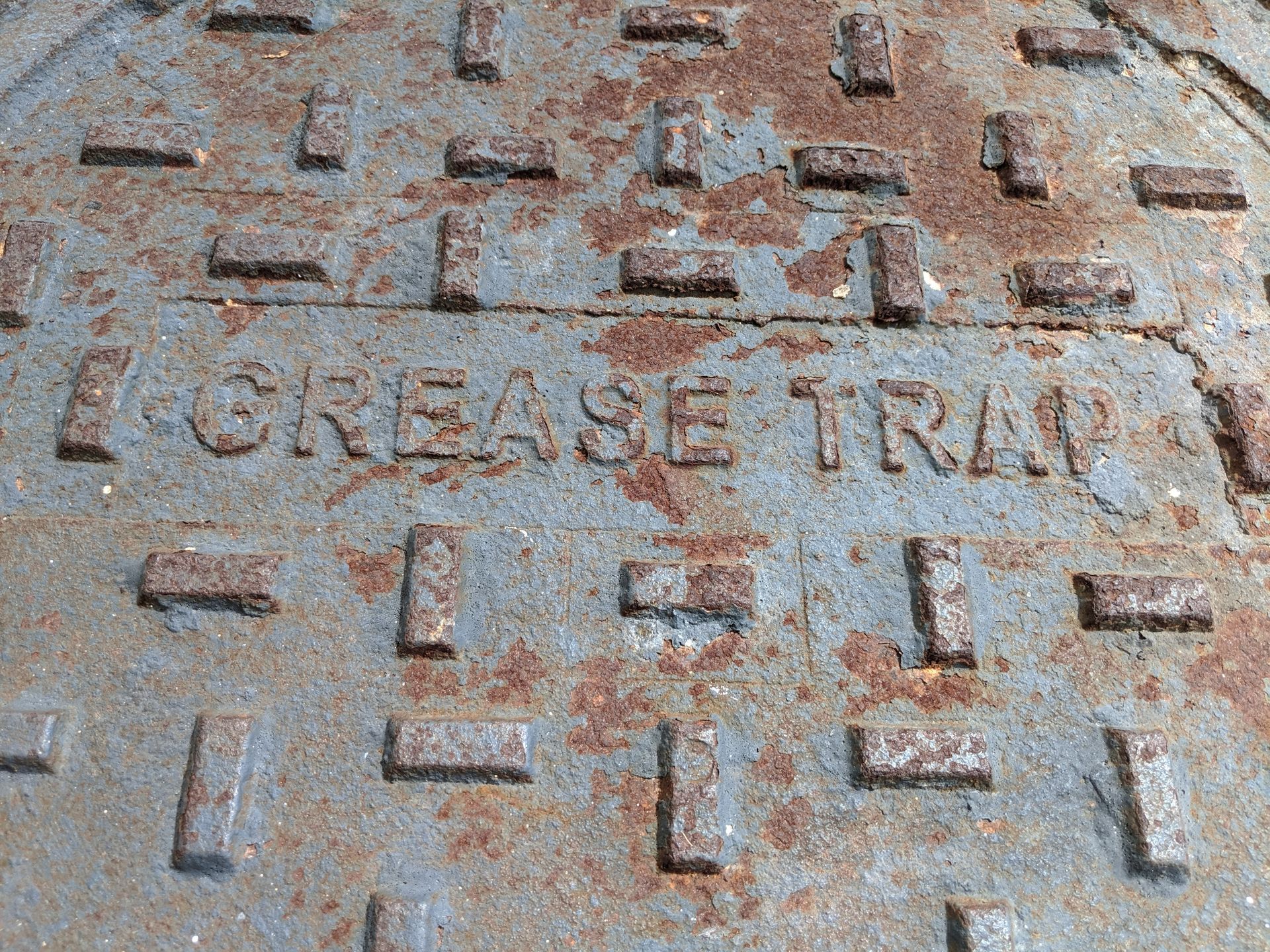 A rusted metal cover labeled “Grease Trap” shows worn textures and raised patterns. A rusted metal cover labeled “Grease Trap” shows worn textures and raised patterns.