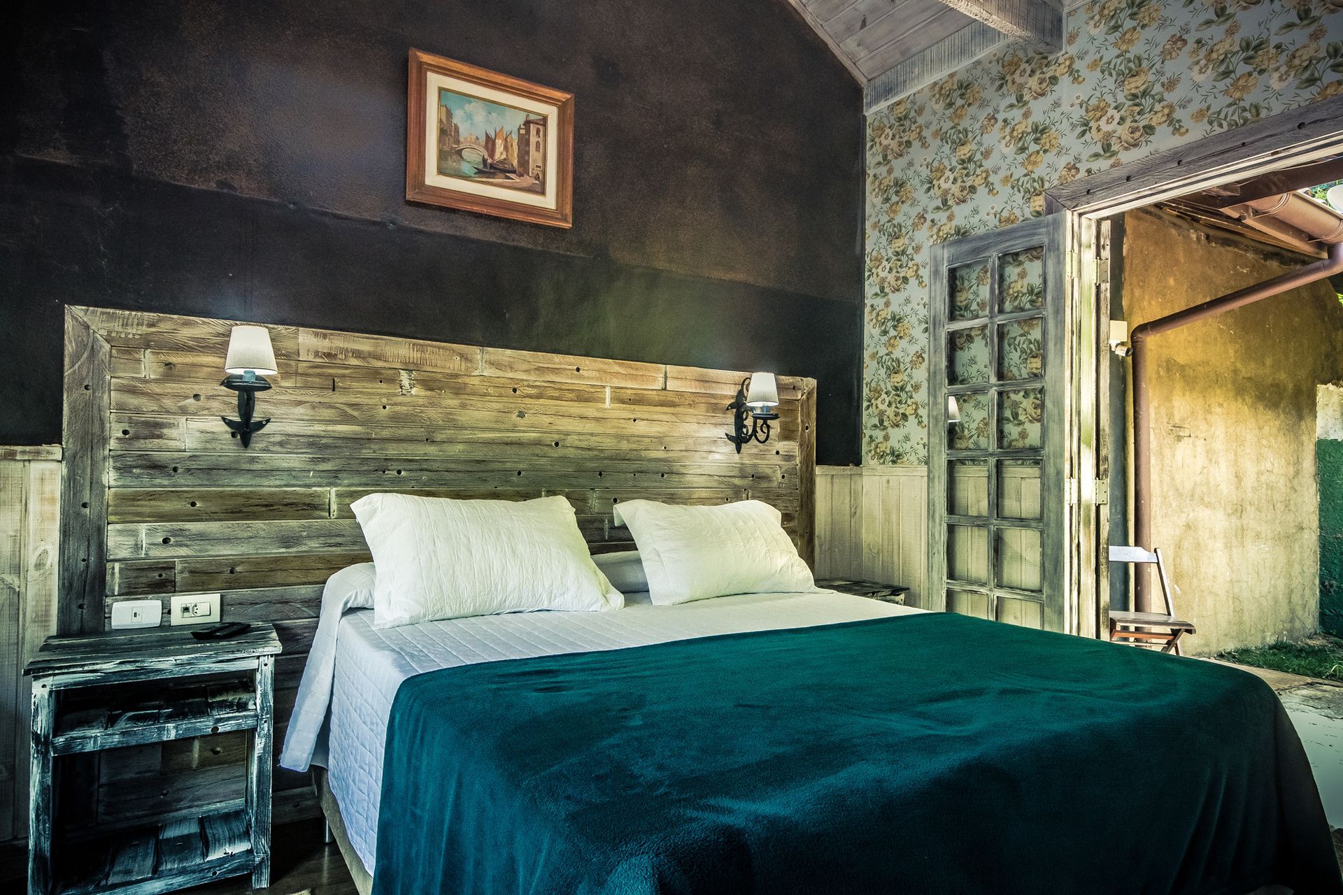 Um quarto com cama, mesa de cabeceira e um quadro na parede.