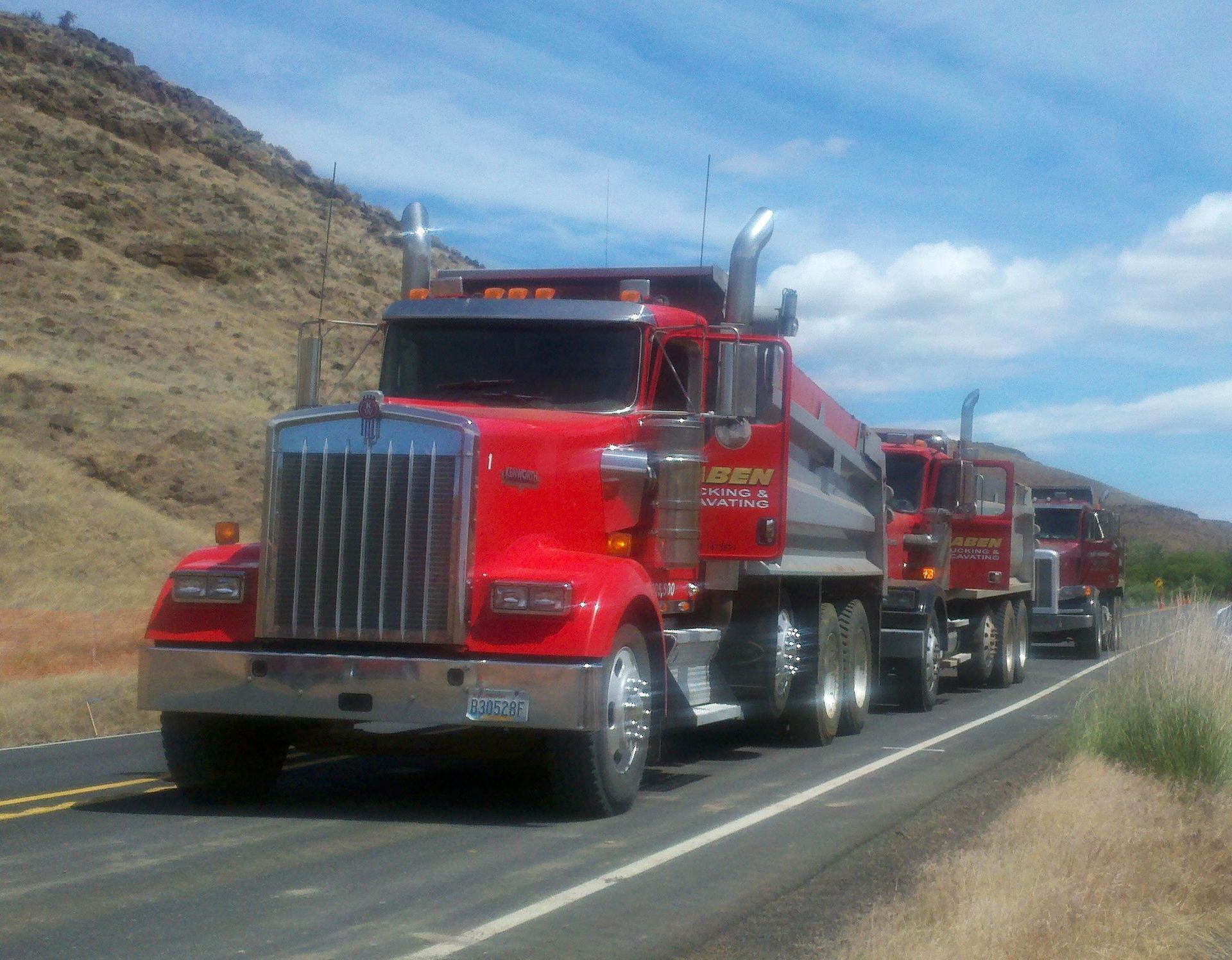A row of red semi trucks are driving down a highway