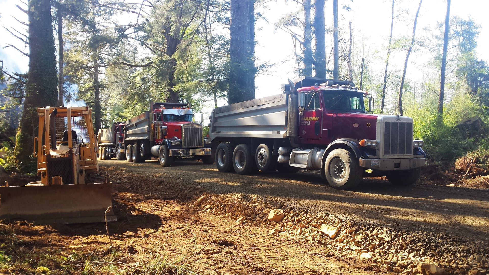 A dump truck is parked on a dirt road next to a bulldozer.
