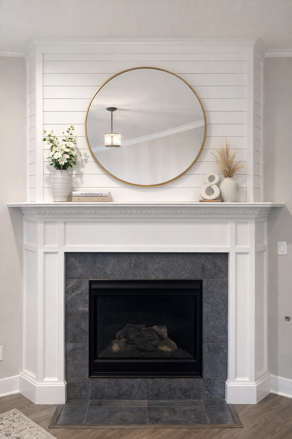 White fireplace with black tiled interior, round mirror, and decorative accents.
