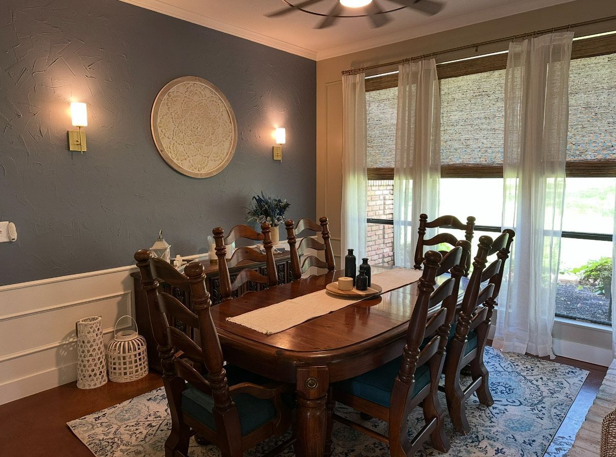 Dining room with wooden table, eight chairs, blue wall, window, rug, and decorative items.